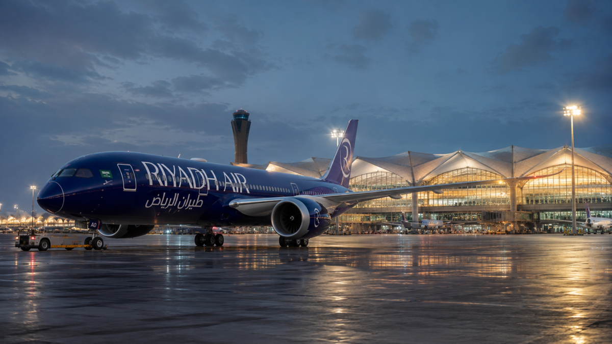A Riyadh Air commercial aircraft parked on the tarmac at King Khalid International Airport under a modern lit terminal roof at dusk.